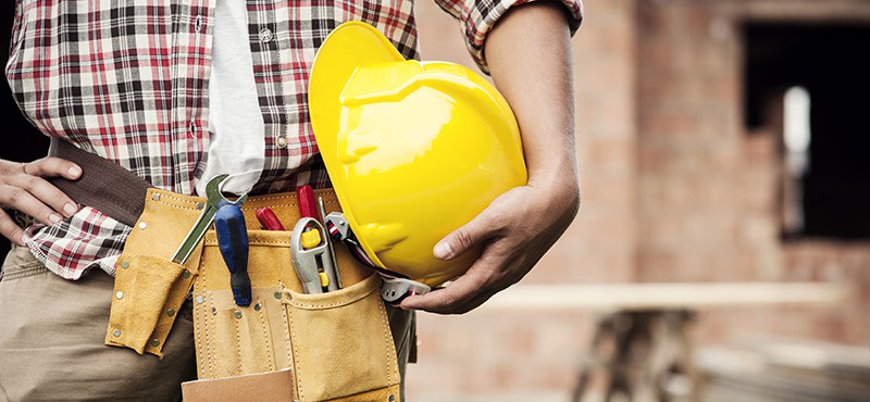 contractor with a tool belt holding a yellow hard hat