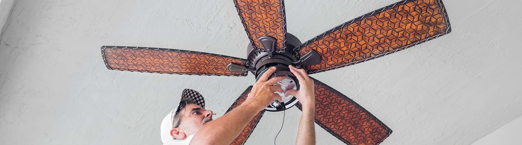 A real electrician stands on a ladder while finishing hanging a ceiling fan.