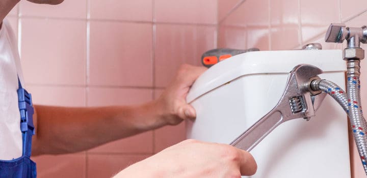 Plumber repairing a toilet pipe with a wrench