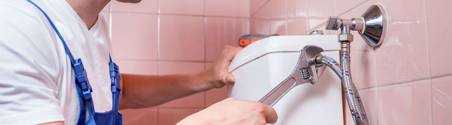 Plumber repairing a toilet pipe with a wrench