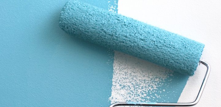 A paint roller covered in teal blue paint, painting over an interior white wall.