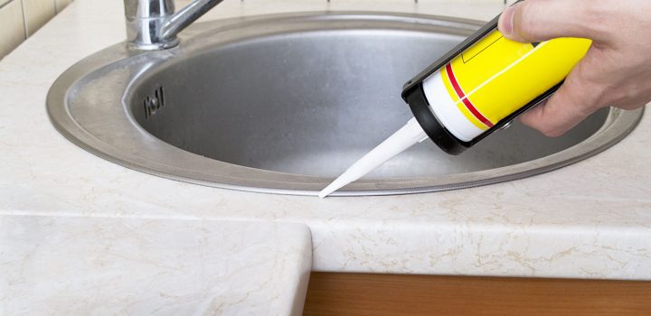 plumber using caulk around a kitchen sink