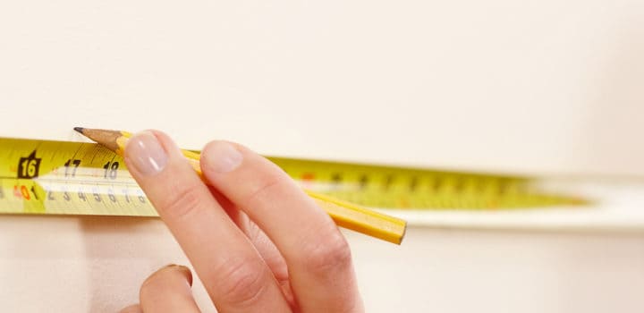 Female worker using tape measure and pencil to make wall markings