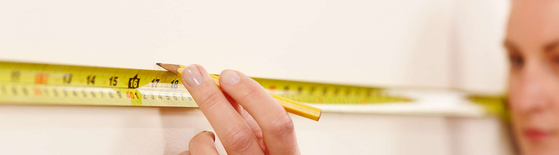 Female worker using tape measure and pencil to make wall markings