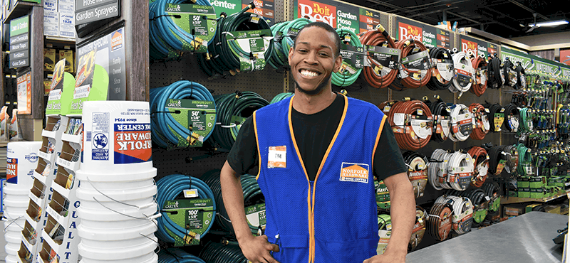 a Norfolk Hardware employee standing in front of a rack of hoses and other garden products