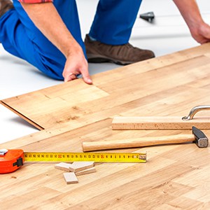 a man installing flooring using a variety of tools including a tape measure, spacers, a mallet and tapping block