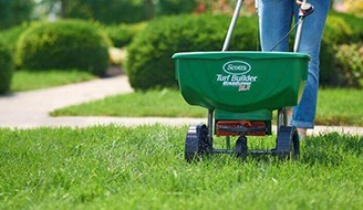 a person spreading lawn fertilizer on grass with a lawn spreader