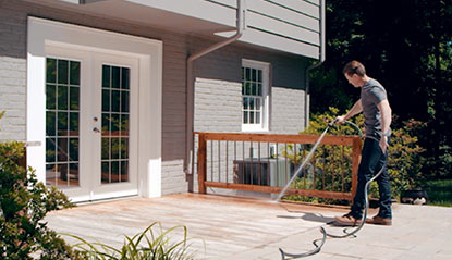 man cleaning deck with hose before applying deck stain