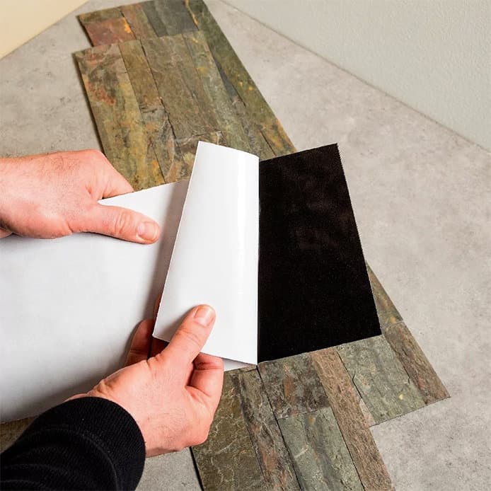 a person peeling off paper to expose the adhesive side of the peel & stick kitchen tile