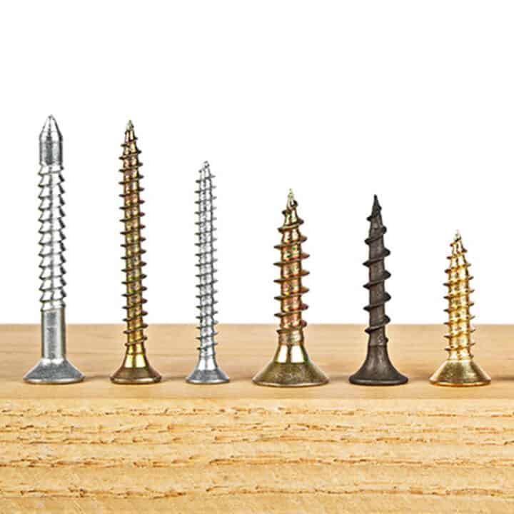 different sizes & shapes of screws lined up in a row on a wood surface