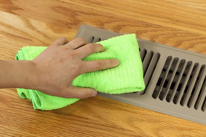 a hand cleaning a brown floor vent