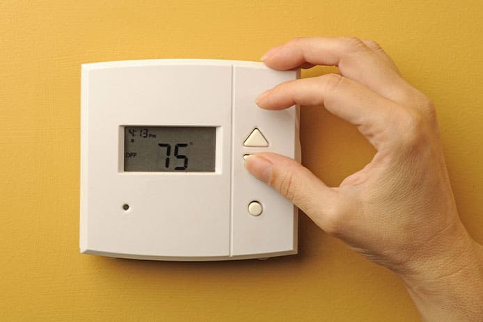 a hand adjusting the temperature of a basic white thermostat